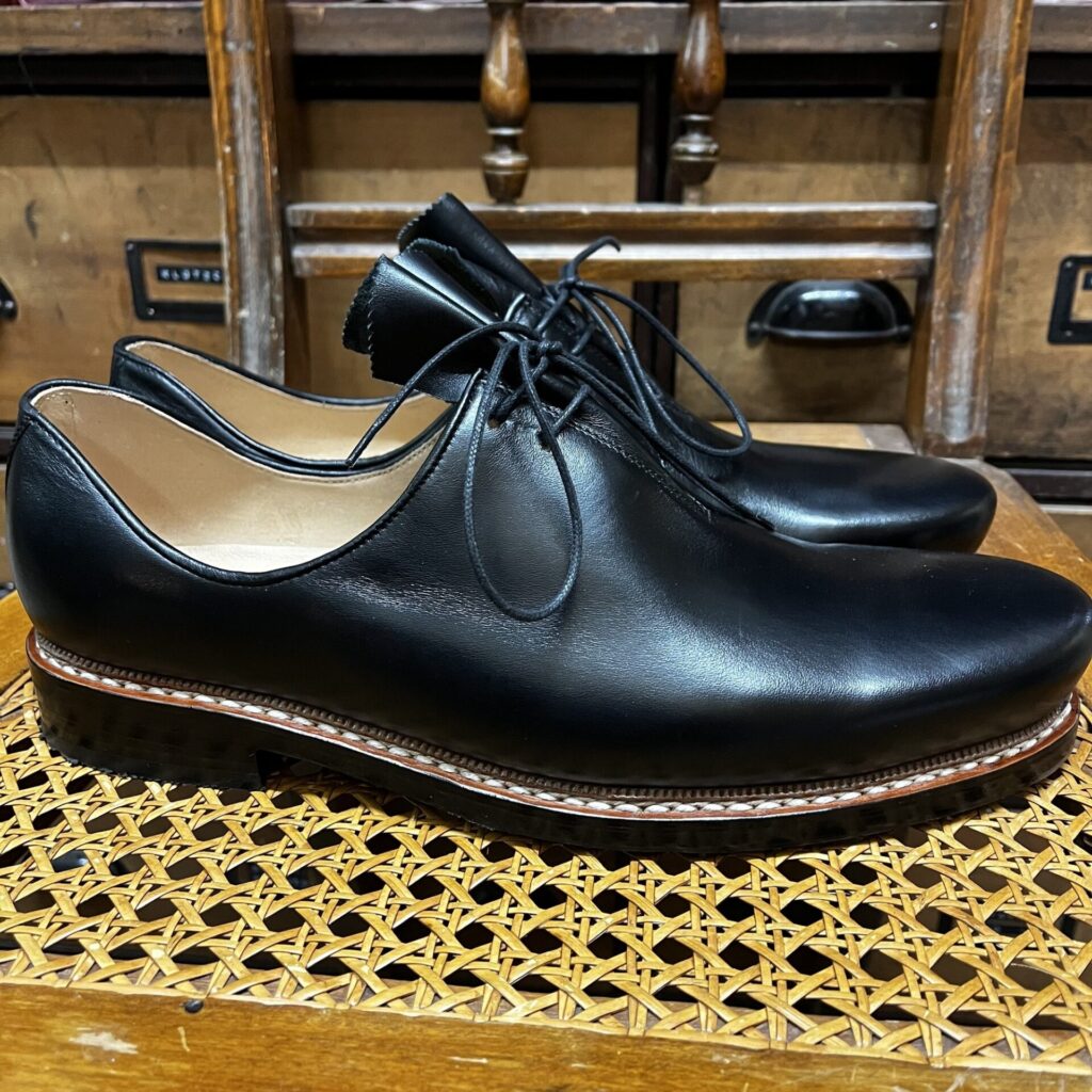 Schwarze Haferlschuhe Schwarze Haferlschuhe mit Mittelschnürung auf einem Geflechtstuhl